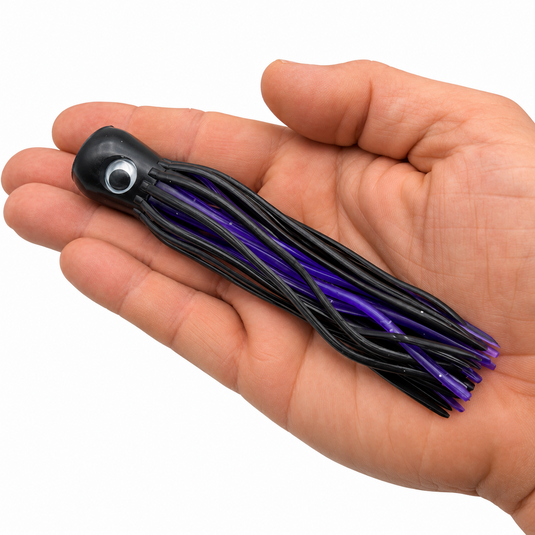 Mold Craft Little Super Chugger 5.5 inch Black/Purple offshore trolling lure shown in hand for size reference, featuring a black head and black-and-purple skirt.